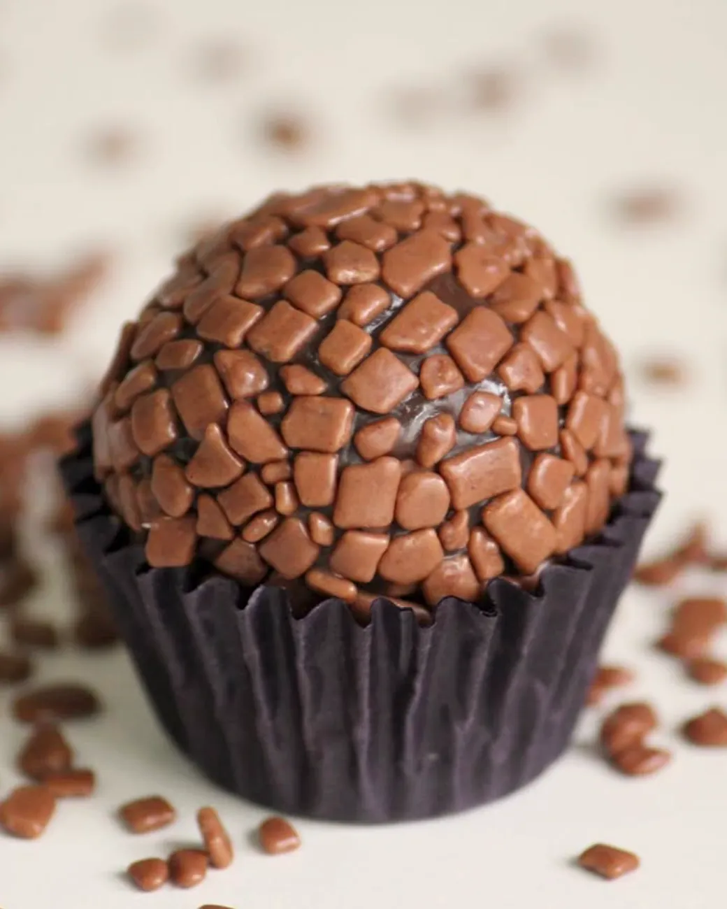 Brigadeiro gourmet da Kathe's Candy coberto de granulado de chocolate, na forminha, com granulado espalhado ao redor